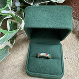 Green jewelry box with a ring featuring colorful gemstones on a textured surface.