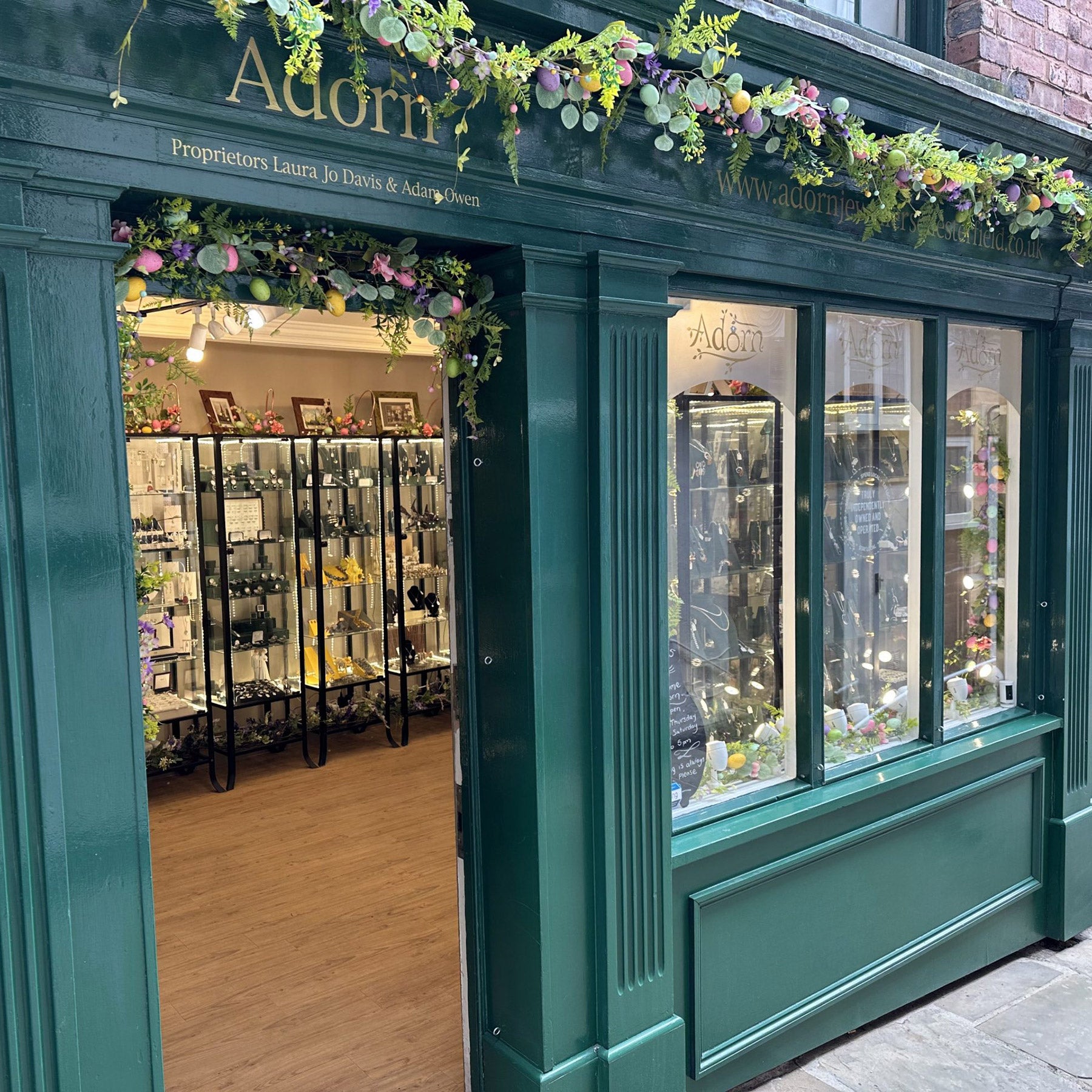 Green storefront with floral decorations and glass windows displaying products