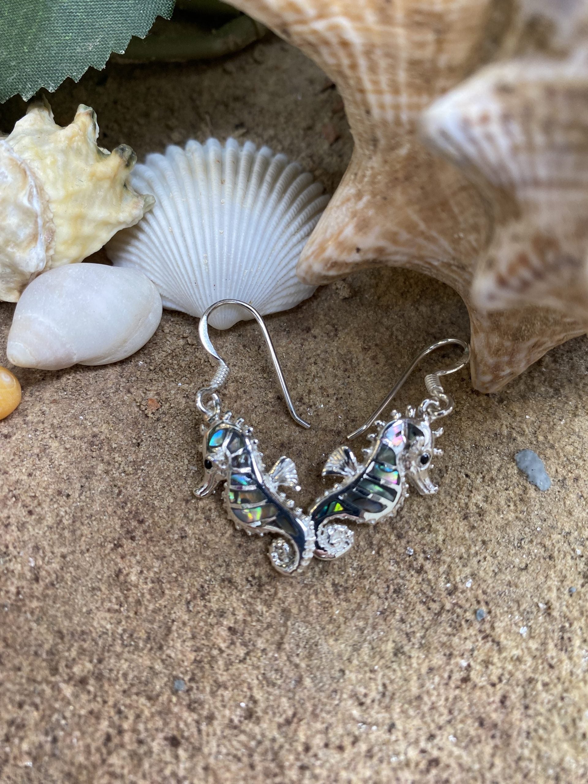 Silver seahorse earrings on sand with shells in the background