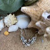 Silver earring with seahorse design on sand with shells and starfish
