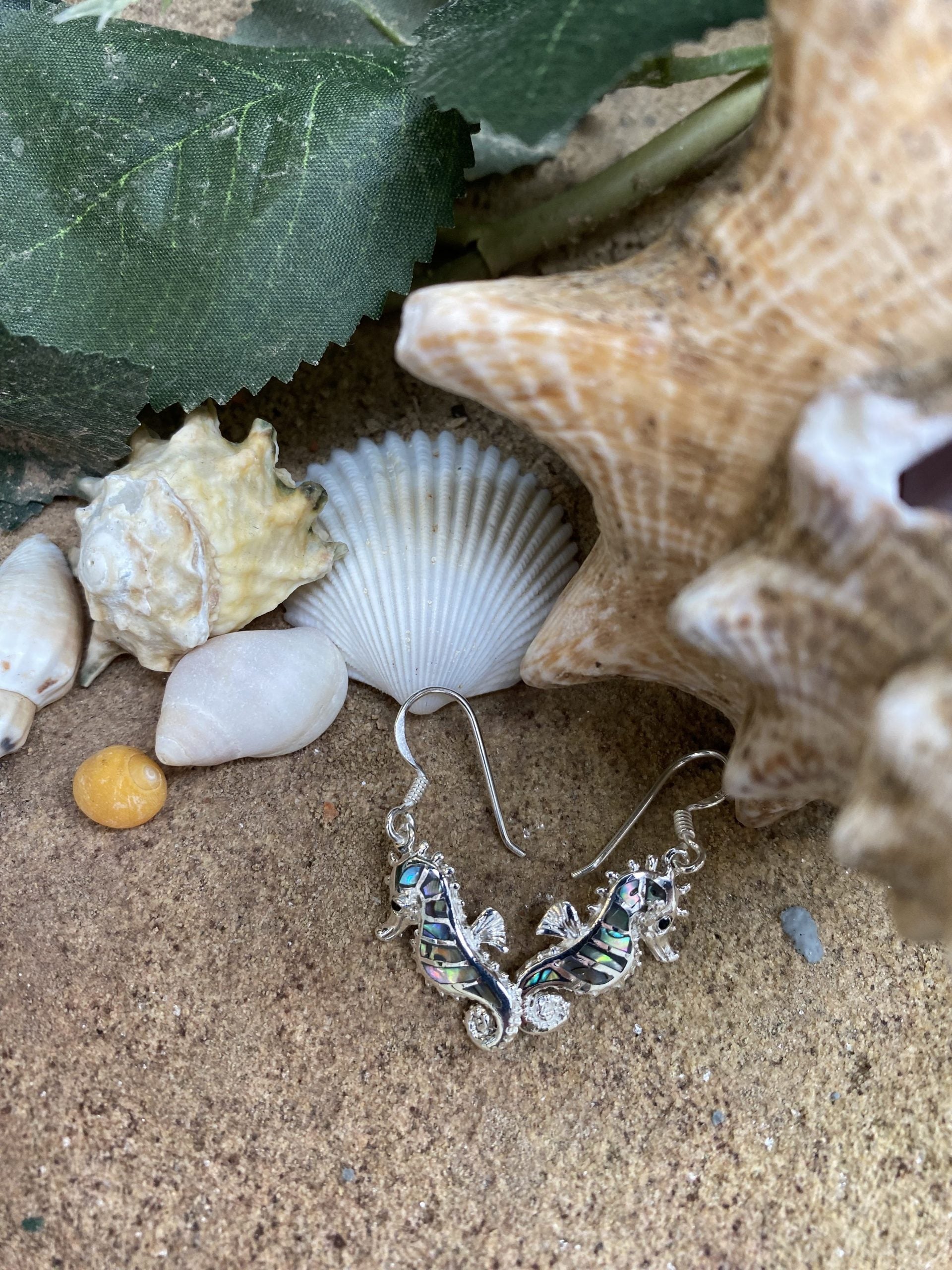 Silver earring with seahorse design on sand with shells and starfish