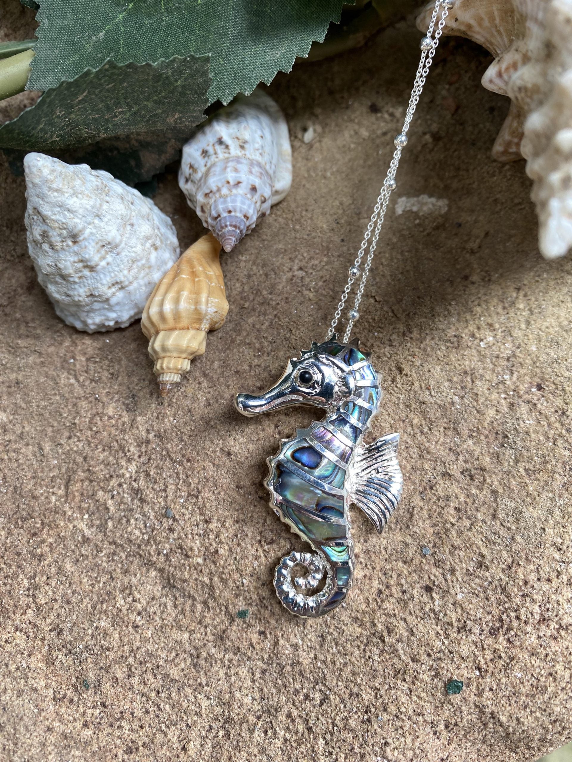 Silver seahorse necklace on sand with shells and leaves
