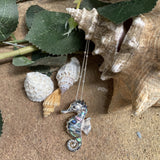Silver seahorse necklace on sand with shells and leaves