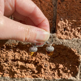 Hand holding a pair of silver earrings with amber beads against a brick wall.