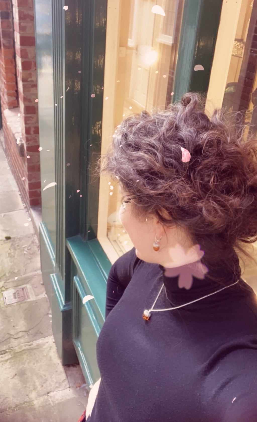 Person with curly hair and earrings standing near a glass door.