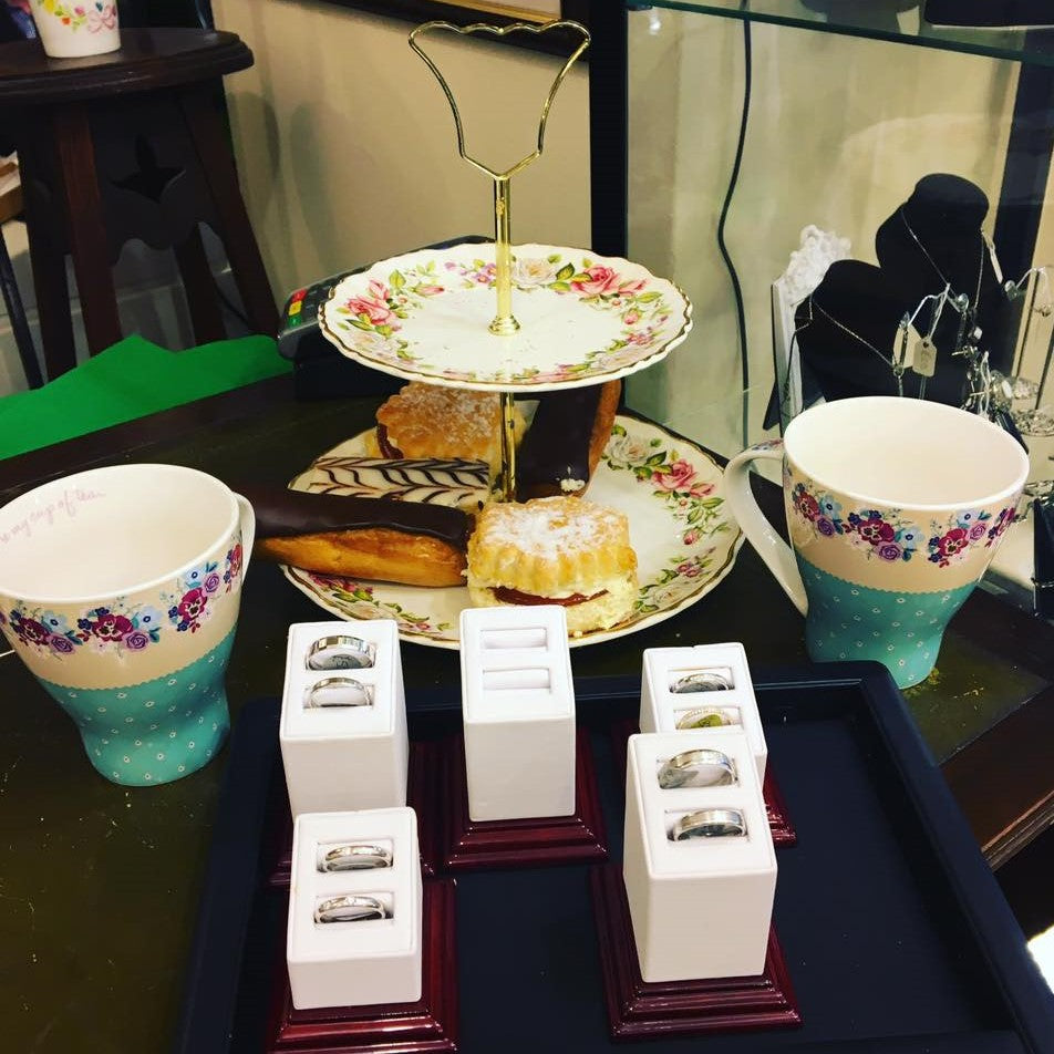 Tea cups with floral designs on a tray with pastries and jewelry boxes.