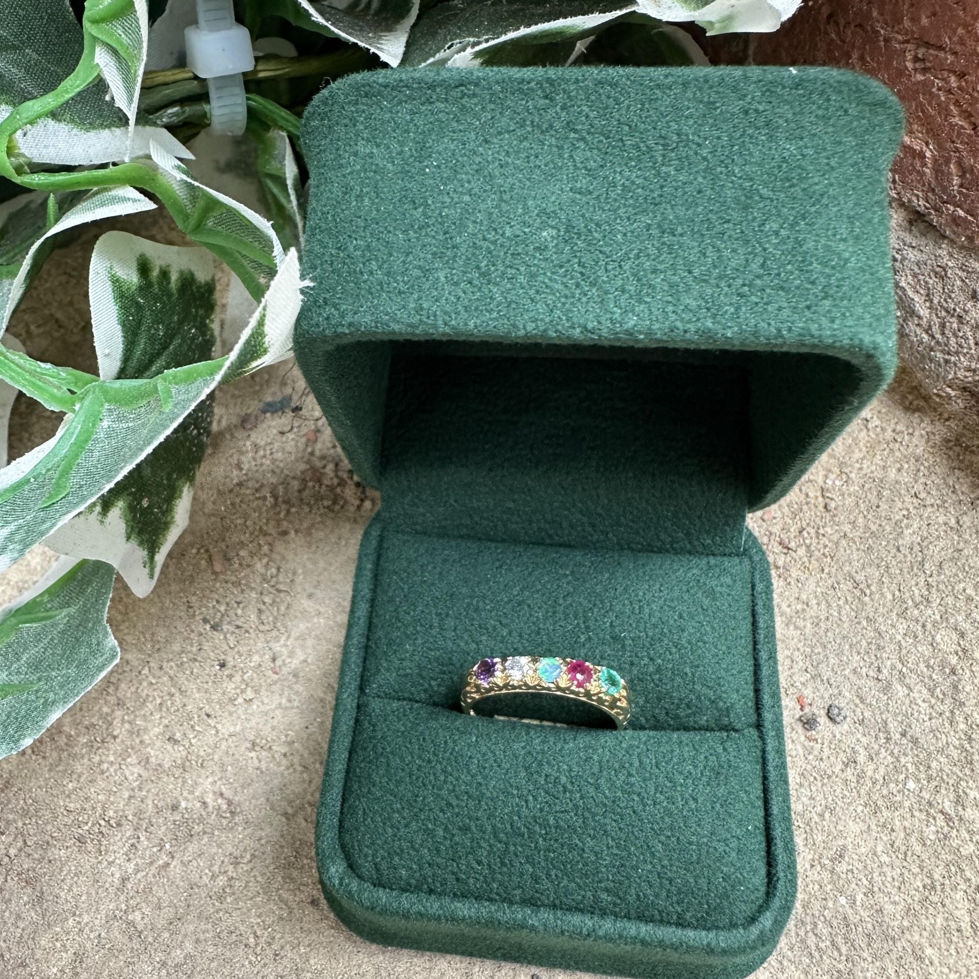 Green jewelry box with a ring featuring colorful gemstones on a textured surface.