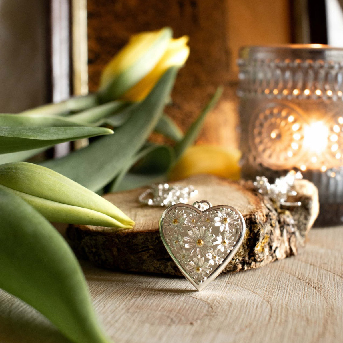 Decorative heart-shaped object on a wooden surface with tulips and a candle in the background