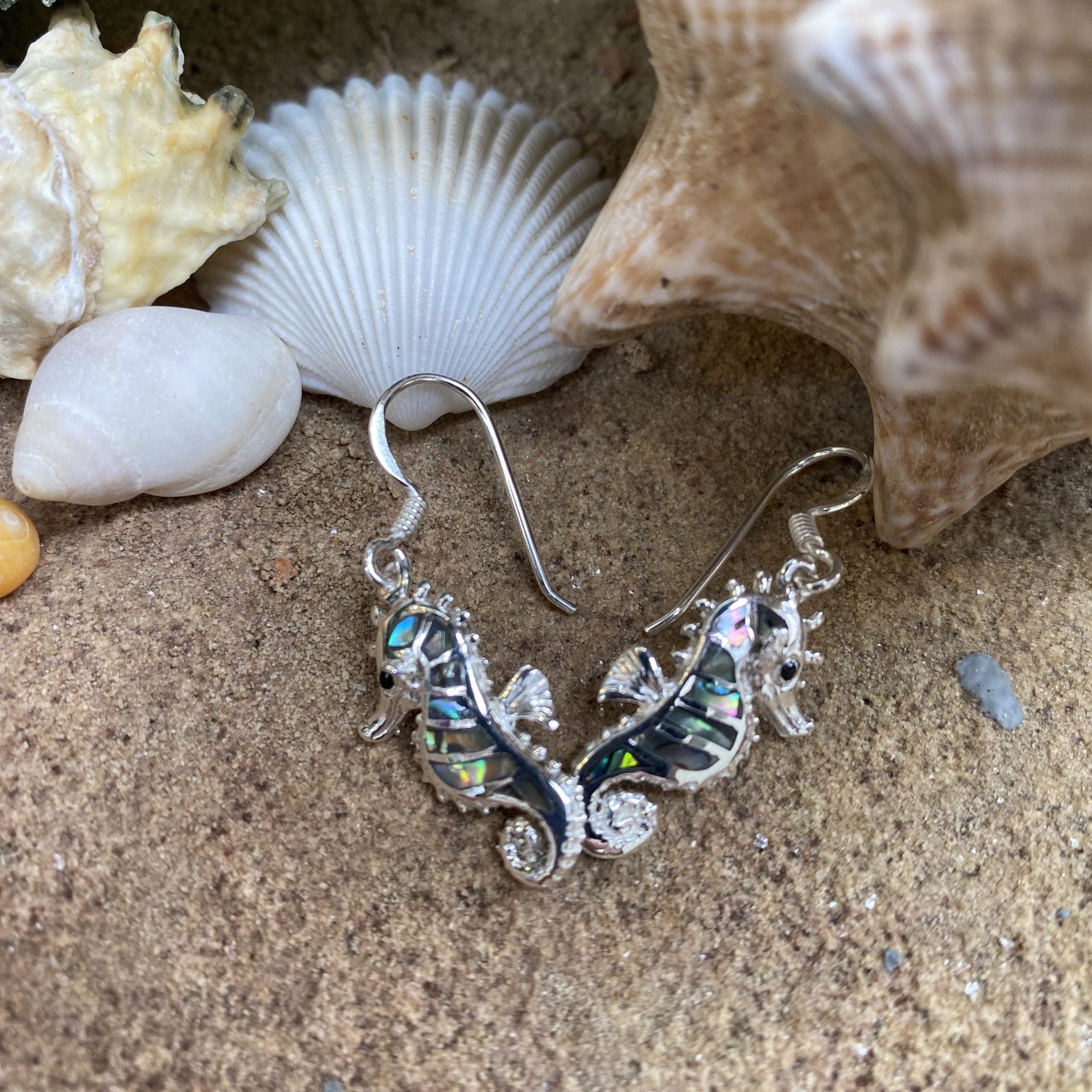 Silver seahorse earrings on sand with shells in the background