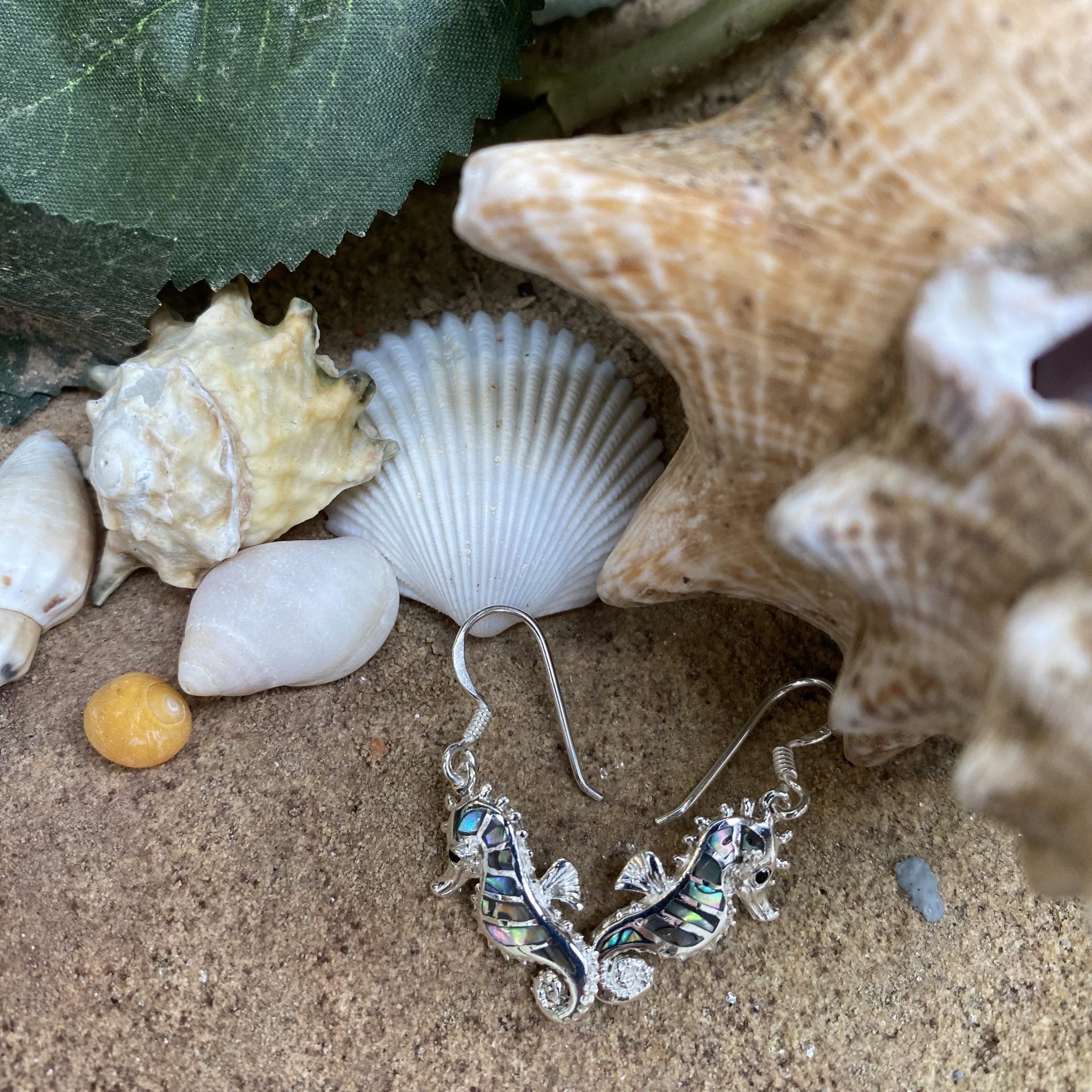 Silver earring with seahorse design on sand with shells and starfish