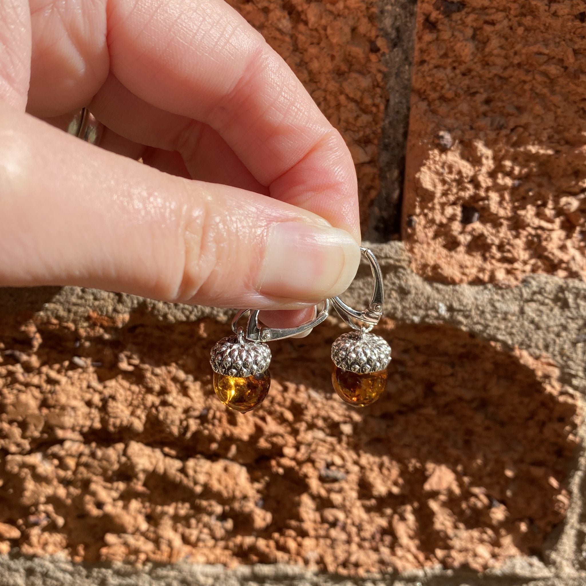 Hand holding a pair of silver earrings with amber beads against a brick wall.