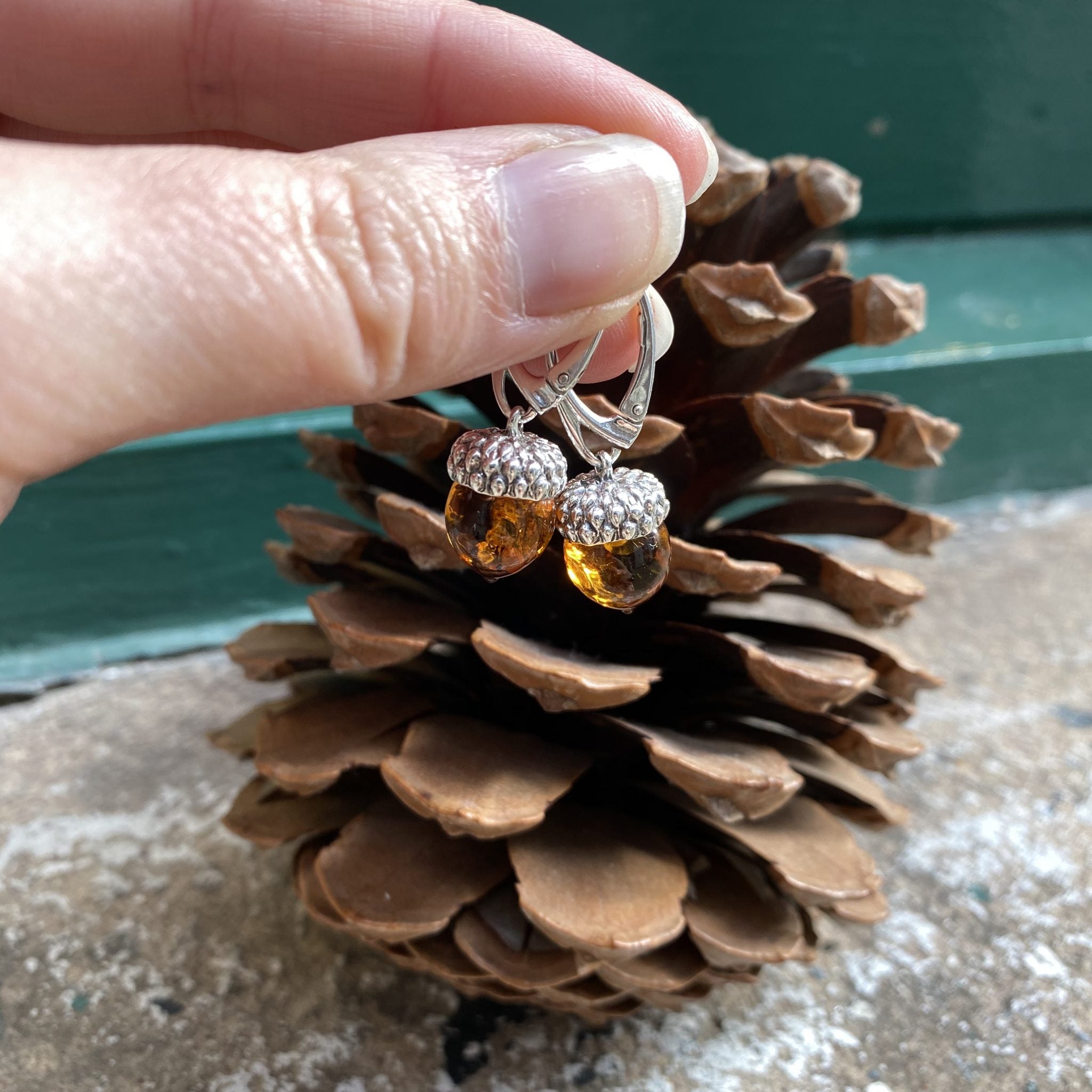 Earrings with amber stones on a pine cone held by a hand.