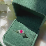 an oval red ruby with three diamonds to either side sits inside an open green velvet box.