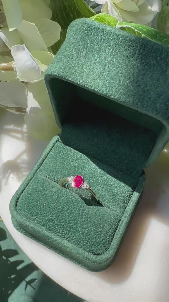 an oval red ruby with three diamonds to either side sits inside an open green velvet box.