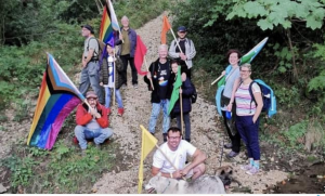 the picture shows a group of people carrying rainbow flags standing and crouched in woodland 